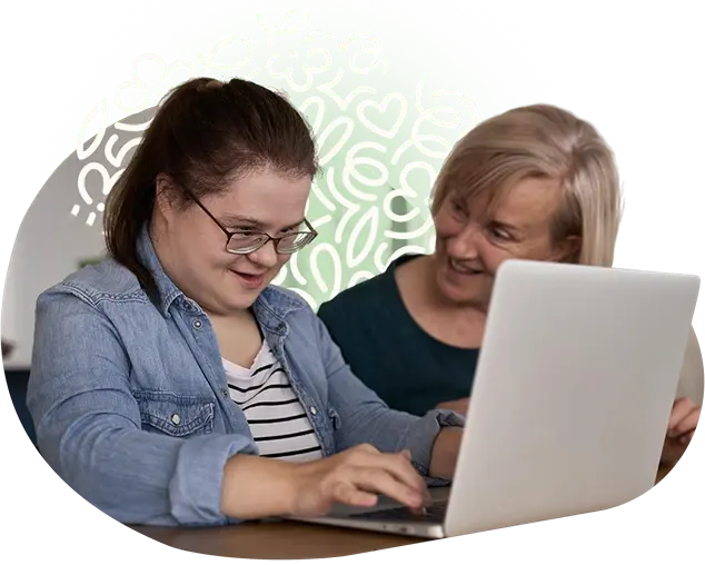 Imagem retratando uma mulher com síndrome de down sendo auxiliada por uma mentora ao usar um computador, representando o cuidado com a rotina do dia a dia dos residentes da clinica de reabilitação Nuren.